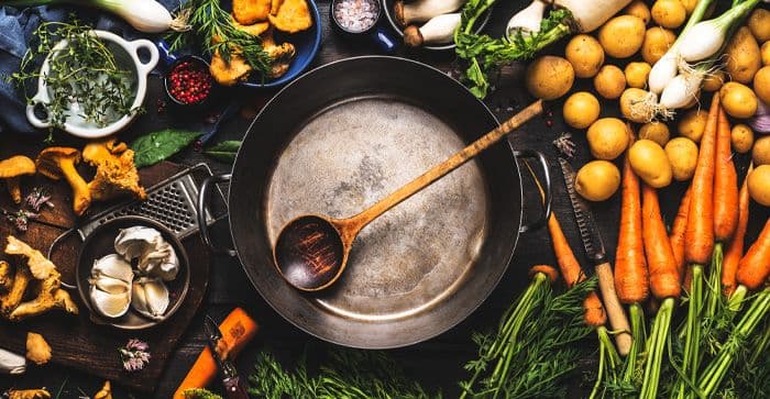 An assortment of vegetables and cooking ingredients laid out on a table with cooking utensils and a frying pan centered in the middle